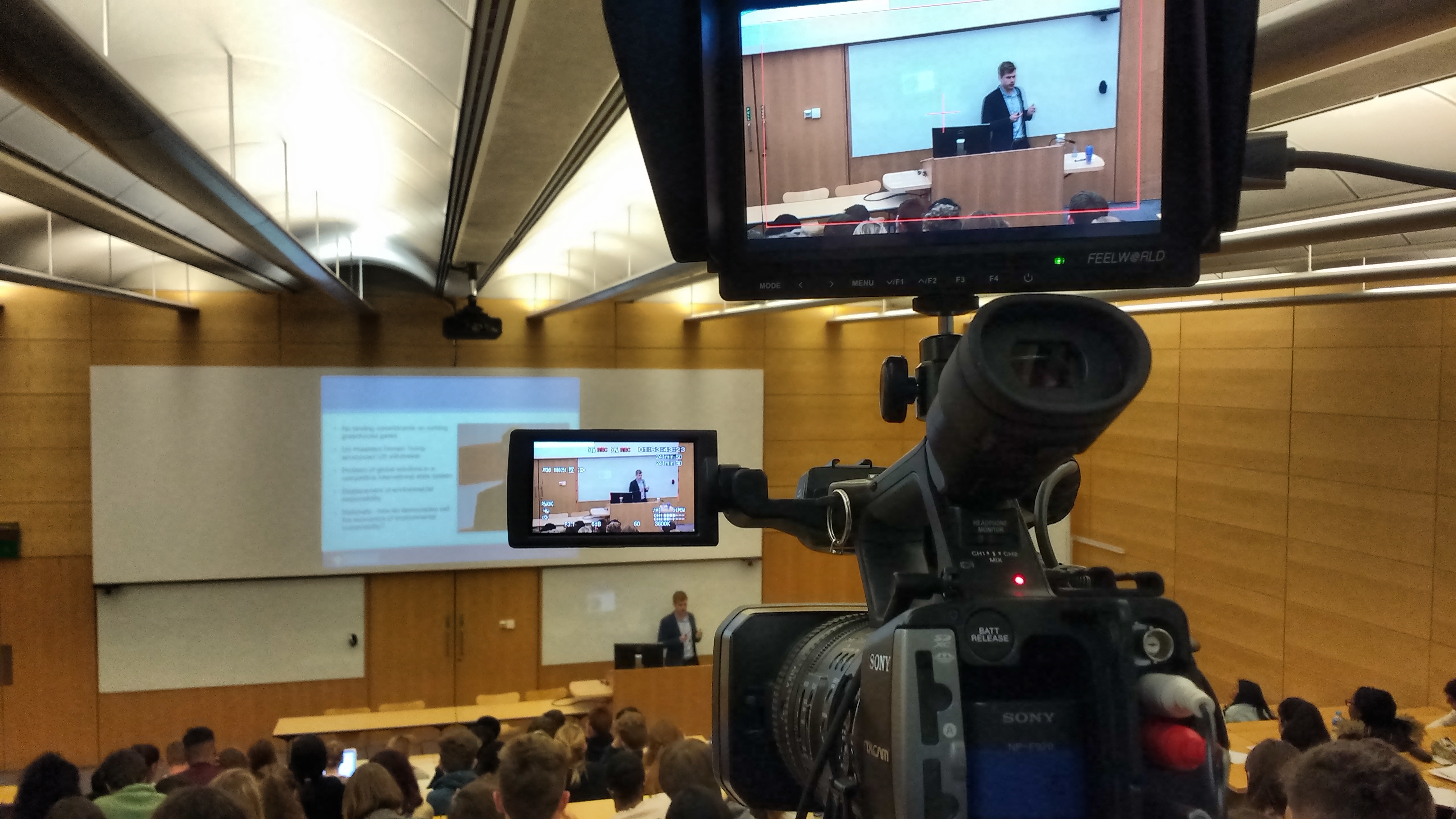 Video camera with large viewfinder looking over a lecture theatre.